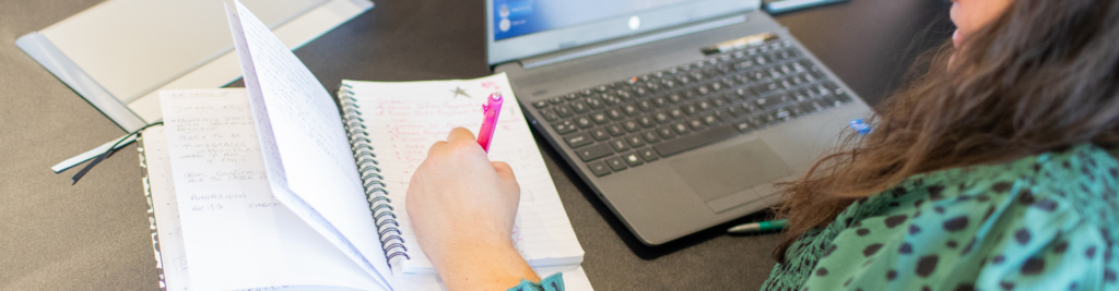 A close up of a desk showing a notepad and pen, and a laptop keyboard